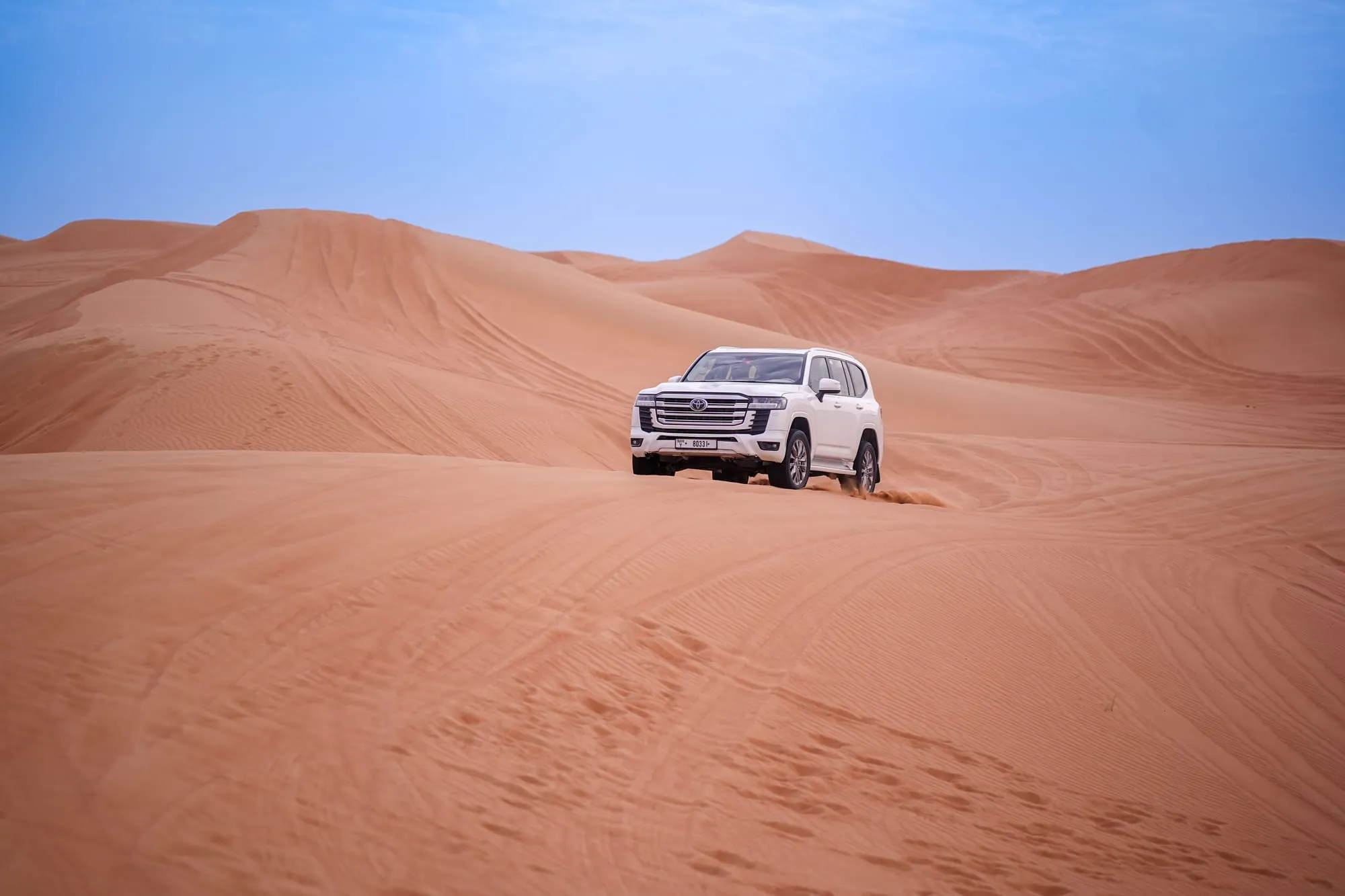 SUV driving across red desert dunes
